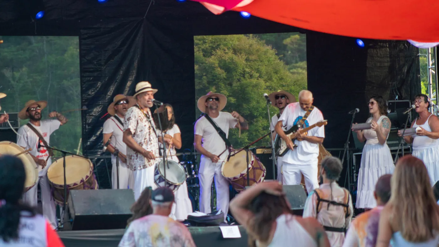 Banda com músicos e cantores vestidos de branco em apresentação no palco com público