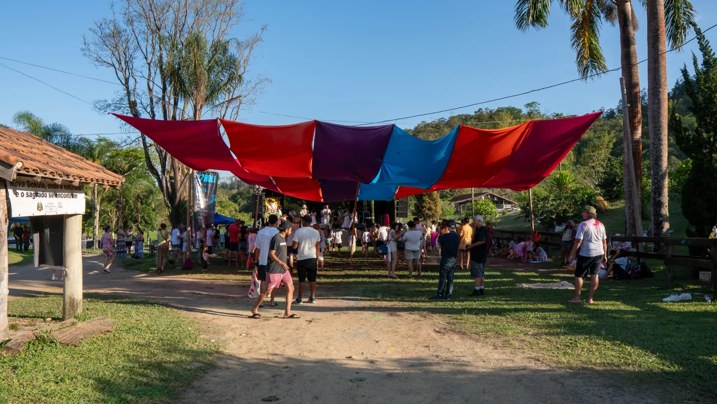 Vista aberta do espaço do festival com tecidos coloridos suspensos, árvores e montanhas ao fundo