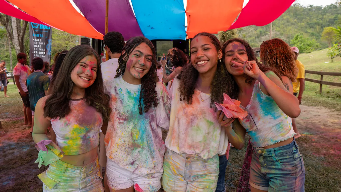 Grupo de amigas cobertas de pó colorido posando abraçadas