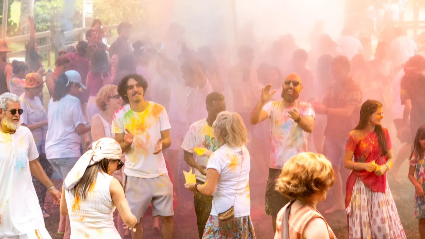 Participantes de branco lançando pó colorido em meio à névoa rosa